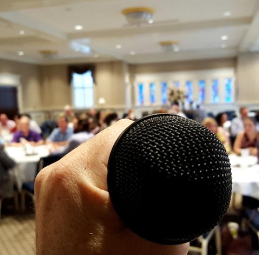 cropped-image-hand-holding-microphone-with-people-sitting-chairs_1048944-25449982